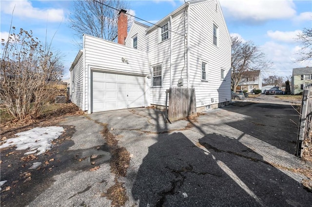 view of property exterior with an attached garage, driveway, and a chimney