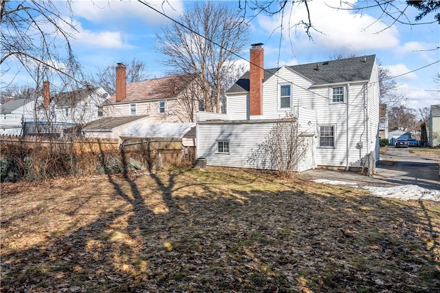 back of house with a chimney and fence