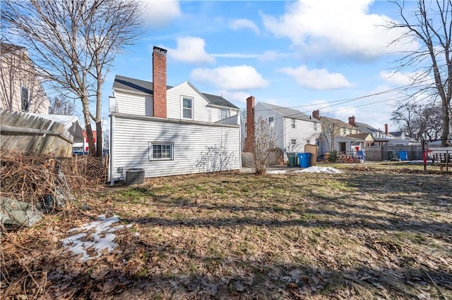 back of property featuring a residential view, central AC unit, a chimney, and fence