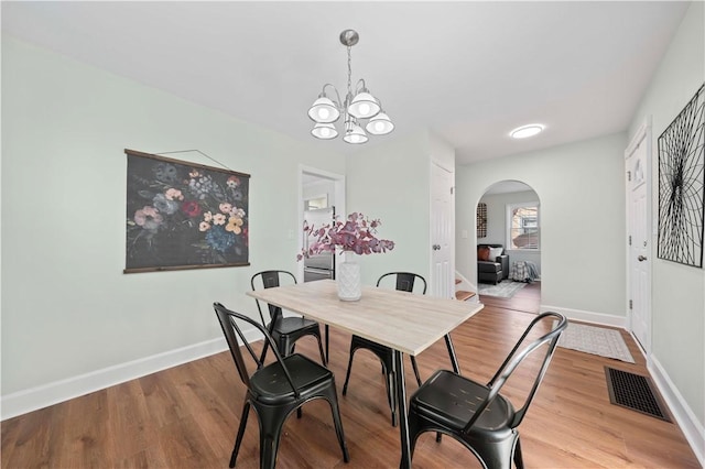 dining space with visible vents, wood finished floors, arched walkways, an inviting chandelier, and baseboards