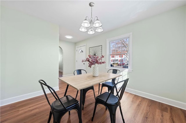 dining space featuring baseboards, arched walkways, a notable chandelier, and wood finished floors