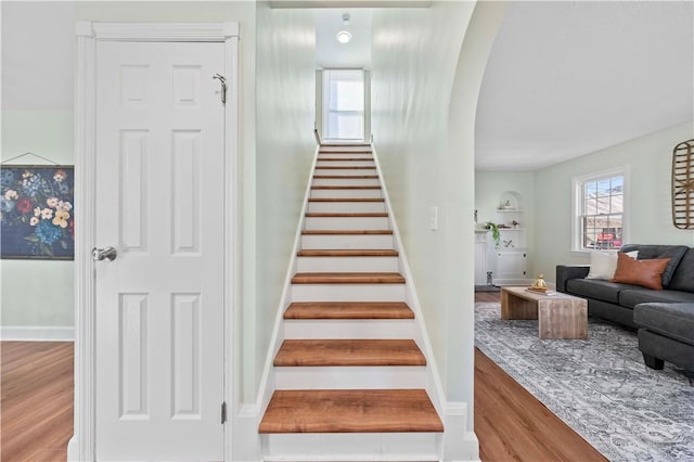 staircase featuring baseboards, arched walkways, and wood finished floors