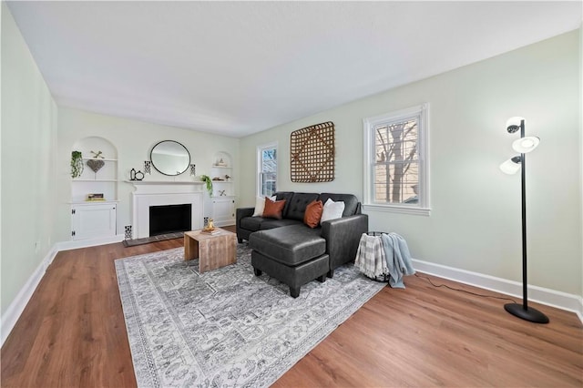 living area featuring built in shelves, a fireplace, baseboards, and wood finished floors