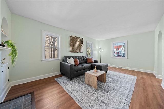 living room with a wealth of natural light, baseboards, arched walkways, and wood finished floors