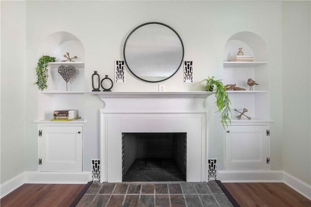 interior details featuring a fireplace with flush hearth, built in shelves, baseboards, and wood finished floors