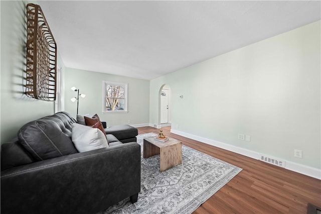 living room with wood finished floors, visible vents, arched walkways, and baseboards