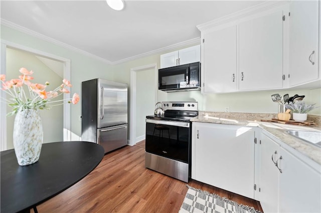 kitchen featuring light stone counters, ornamental molding, white cabinets, light wood-style floors, and appliances with stainless steel finishes