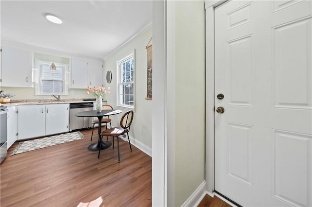 kitchen with dark wood finished floors, light countertops, ornamental molding, white cabinets, and stainless steel dishwasher