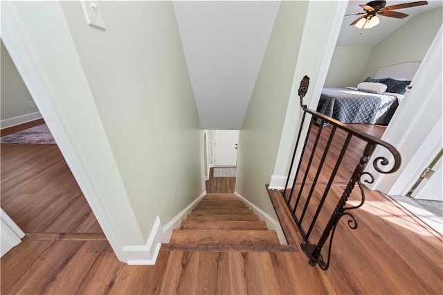 stairs with lofted ceiling, wood finished floors, baseboards, and ceiling fan