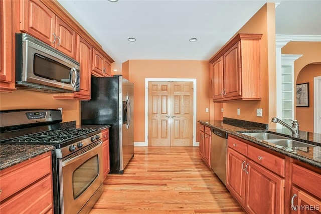 kitchen featuring light wood-type flooring, dark stone counters, a sink, stainless steel appliances, and brown cabinets