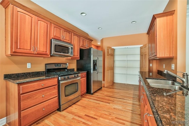 kitchen with dark stone countertops, appliances with stainless steel finishes, light wood-style floors, brown cabinetry, and a sink