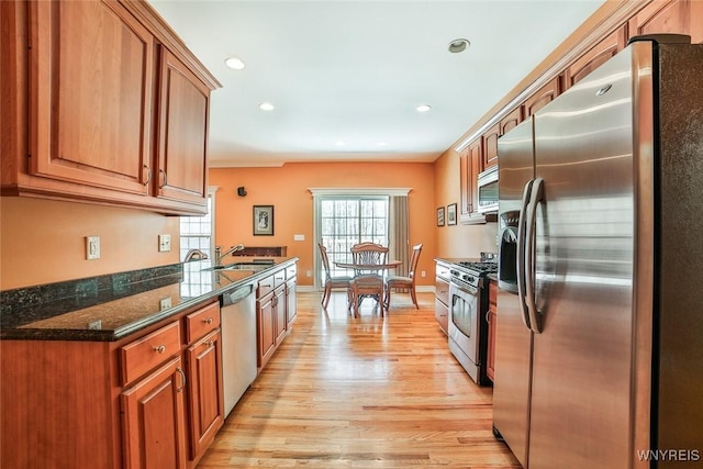 kitchen with brown cabinetry, stainless steel appliances, light wood-style floors, and a sink