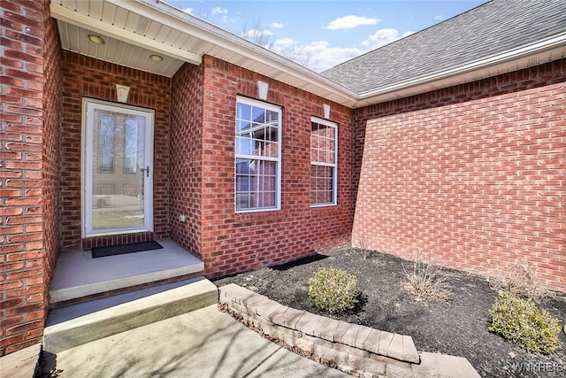 doorway to property with brick siding and a shingled roof