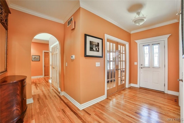 foyer with crown molding, light wood-style flooring, french doors, and arched walkways