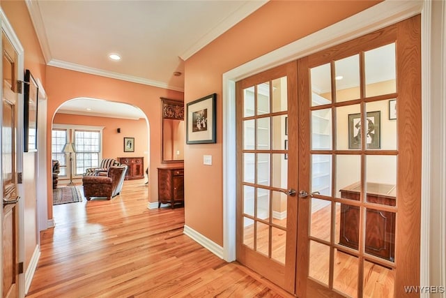 interior space with baseboards, light wood finished floors, arched walkways, french doors, and crown molding