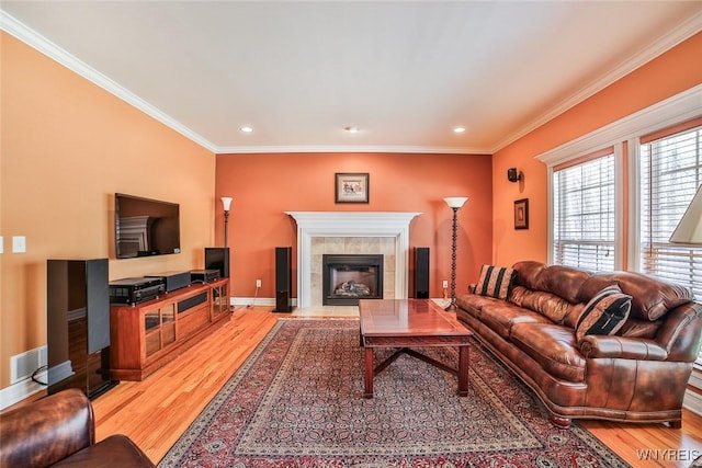 living area with a tiled fireplace, visible vents, light wood-style flooring, and ornamental molding