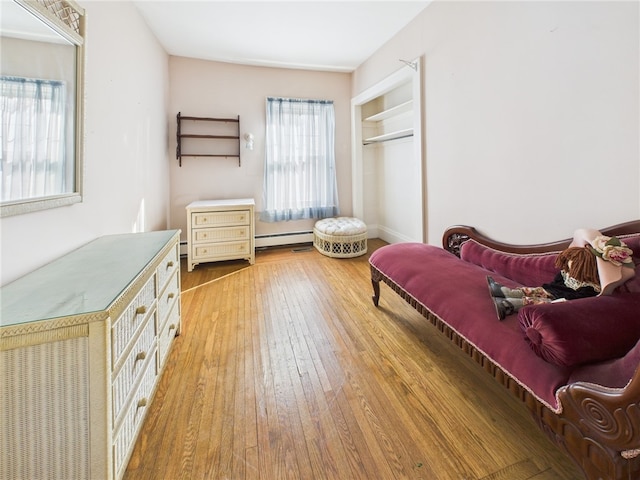 bedroom with a closet, a baseboard heating unit, and light wood-type flooring