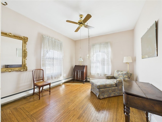 sitting room with a healthy amount of sunlight, a baseboard heating unit, a ceiling fan, and wood-type flooring