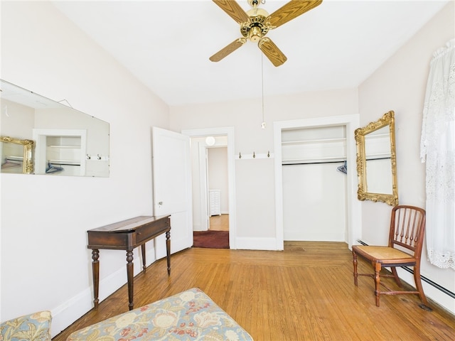 living area with a ceiling fan, light wood-style floors, baseboards, and baseboard heating