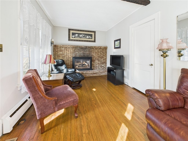 living room featuring ornamental molding, a brick fireplace, wood finished floors, and a baseboard radiator