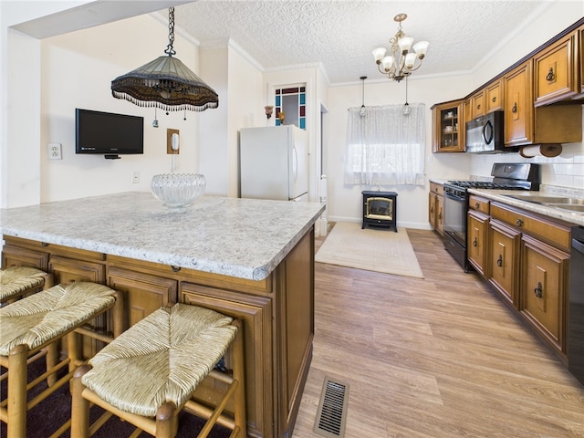 kitchen featuring visible vents, ornamental molding, light wood-style flooring, brown cabinetry, and black appliances