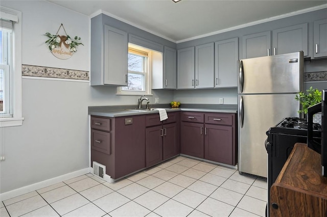 kitchen featuring visible vents, baseboards, light tile patterned floors, freestanding refrigerator, and a sink