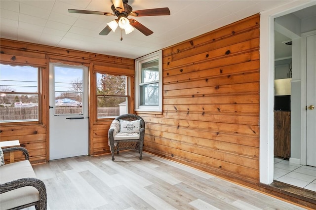 unfurnished room with a wealth of natural light, light wood-style flooring, wood walls, and ceiling fan