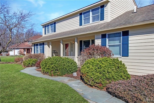 view of front of house with covered porch, a front lawn, and a shingled roof