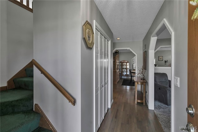 hallway featuring arched walkways, stairway, dark wood finished floors, and a textured ceiling