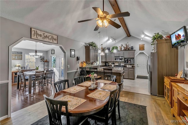 dining space with arched walkways, a textured ceiling, vaulted ceiling with beams, and light wood-style floors