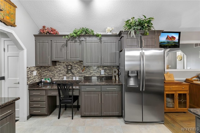 kitchen with backsplash, dark stone counters, a textured ceiling, and stainless steel refrigerator with ice dispenser