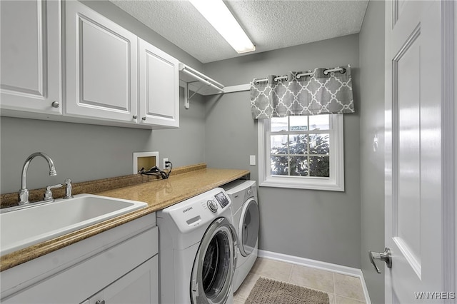 laundry area featuring washing machine and dryer, light tile patterned floors, cabinet space, a textured ceiling, and a sink