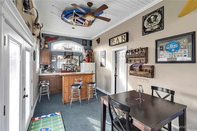 dining room with crown molding, baseboards, ceiling fan, dark carpet, and a dry bar