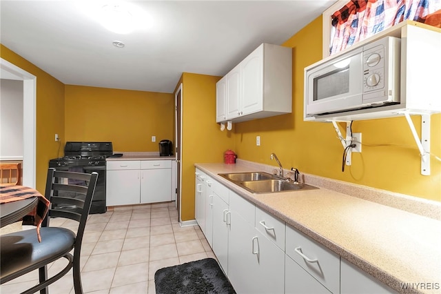 kitchen with white microwave, black range with gas stovetop, light tile patterned flooring, white cabinetry, and a sink