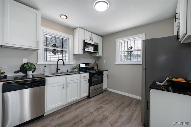 kitchen featuring dark countertops, wood finished floors, white cabinets, stainless steel appliances, and a sink