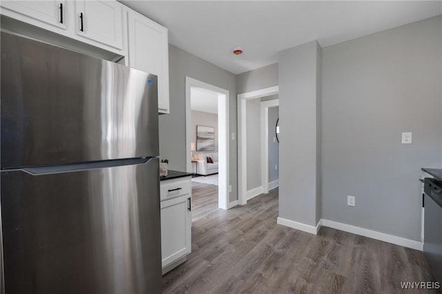 kitchen with dark countertops, wood finished floors, white cabinetry, stainless steel appliances, and baseboards