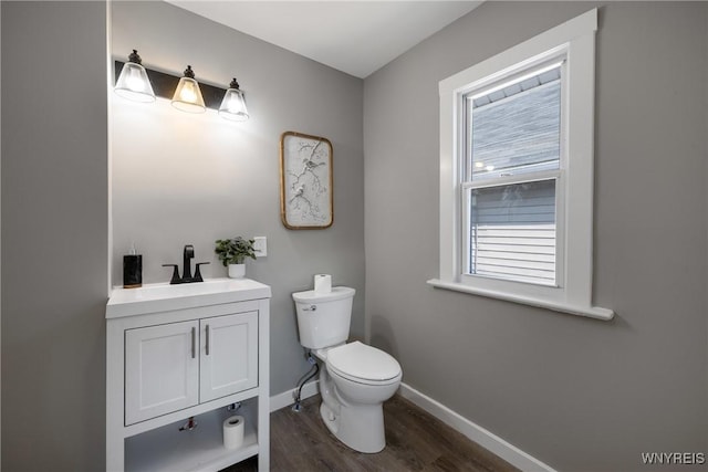 half bath with vanity, toilet, wood finished floors, and baseboards