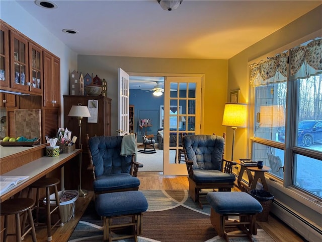 sitting room with french doors, light wood-type flooring, a ceiling fan, and a baseboard radiator