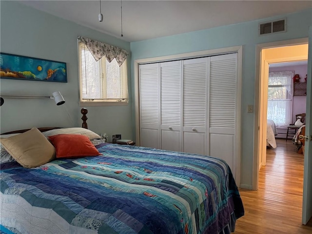 bedroom with visible vents, multiple windows, a closet, and wood finished floors