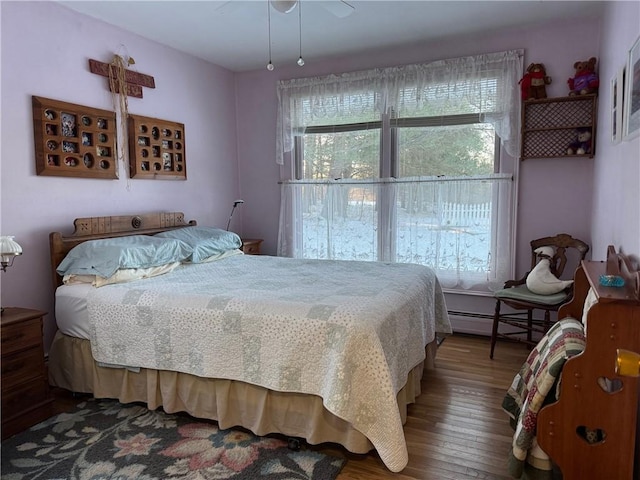 bedroom with hardwood / wood-style floors, multiple windows, ceiling fan, and a baseboard radiator