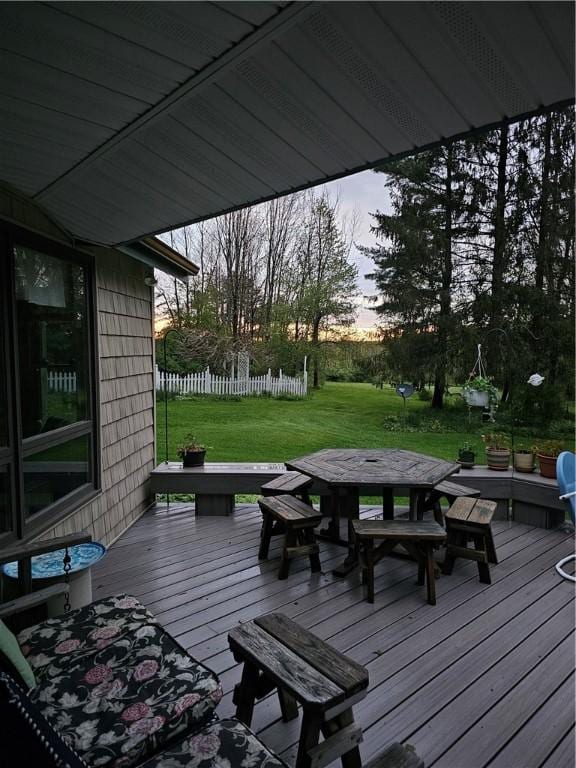 deck at dusk with outdoor dining area, a yard, and fence