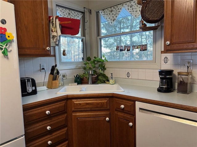 kitchen with decorative backsplash, white appliances, light countertops, and a sink