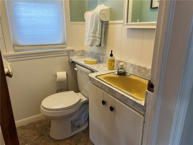 half bath with tile patterned flooring, wainscoting, toilet, and vanity