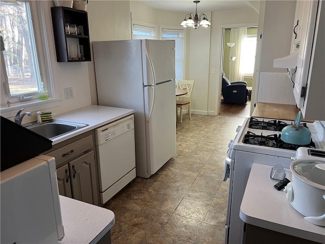 kitchen featuring baseboards, light countertops, a notable chandelier, white appliances, and a sink