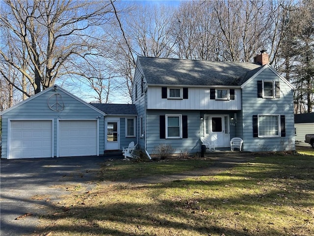 view of front of house featuring a front yard, roof with shingles, driveway, a chimney, and a garage