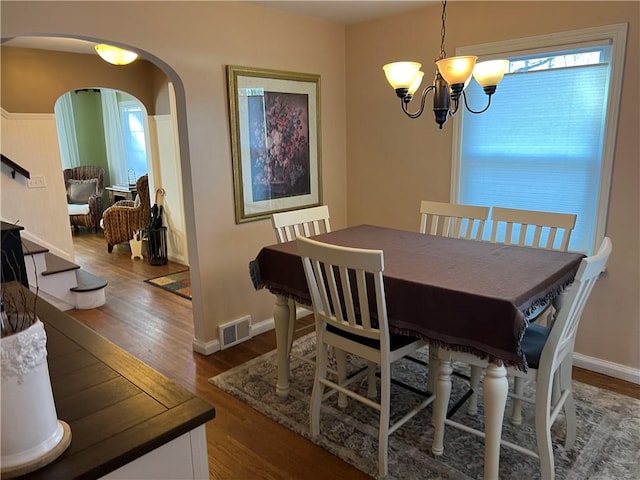 dining room with visible vents, wood finished floors, arched walkways, an inviting chandelier, and stairs