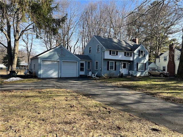 colonial home with aphalt driveway, an attached garage, a chimney, and a front yard