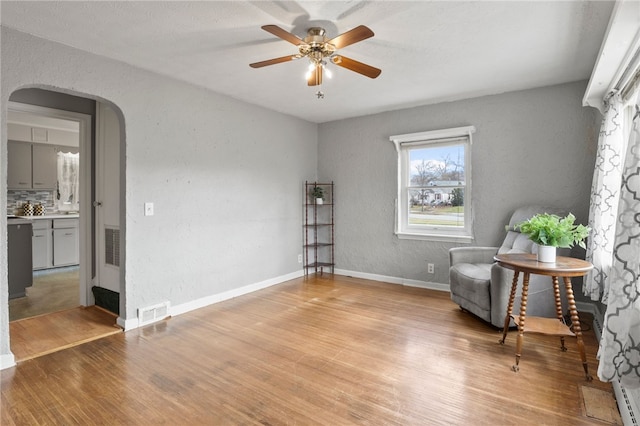 sitting room featuring baseboards, light wood-type flooring, arched walkways, and visible vents