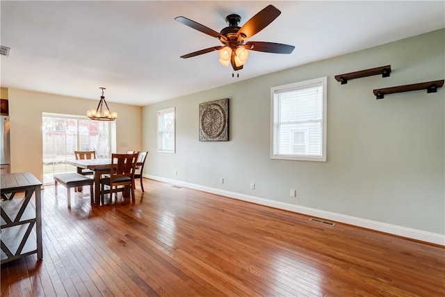 dining area with visible vents, wood-type flooring, baseboards, and ceiling fan with notable chandelier