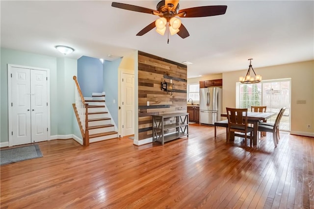 dining space featuring stairway, ceiling fan with notable chandelier, baseboards, and light wood finished floors